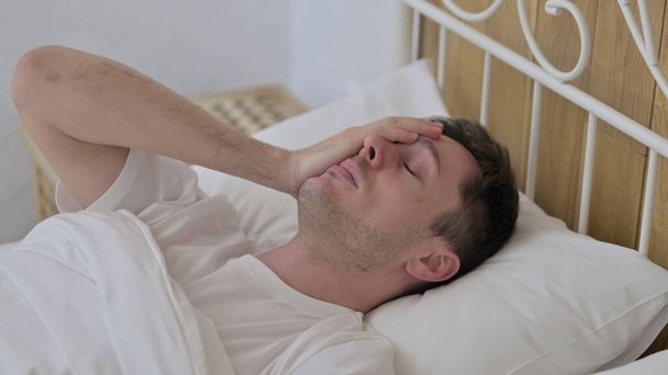Молодий чоловік прокидається зі сну в ліжку
 - Фото, зображення