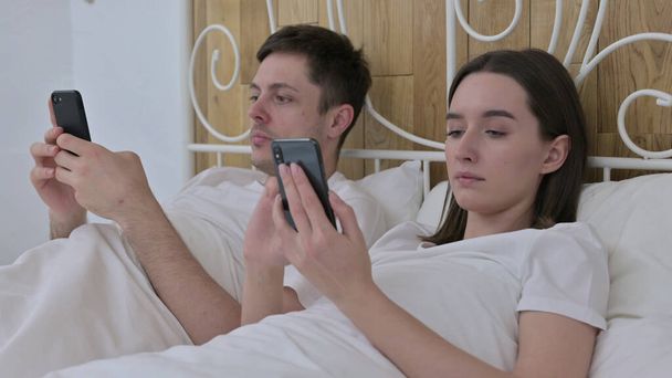 ベッドの中でスマートフォンを使用して魅力的なカップル - 写真・画像