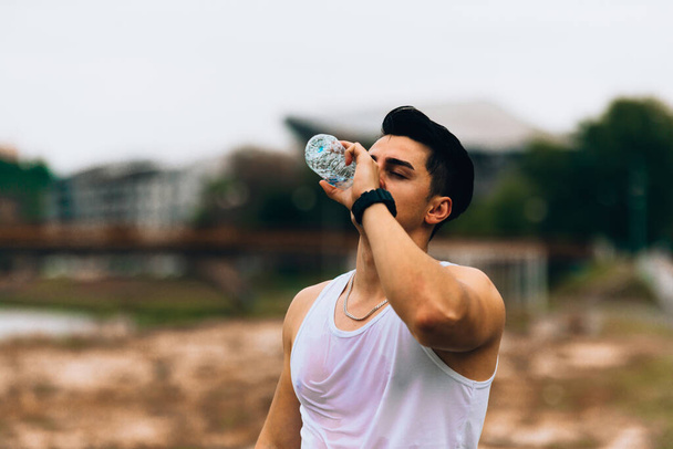 Young exhausted athlete drinking fresh water to refresh during a running trail - Photo, image