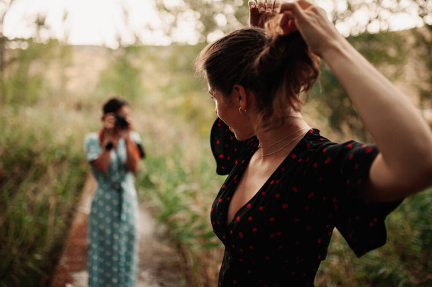 Δύο νεαρές γυναίκες τραβάνε φωτογραφίες η μία την άλλη στο δάσος ανάμεσα στα δέντρα φορώντας φορέματα. - Φωτογραφία, εικόνα