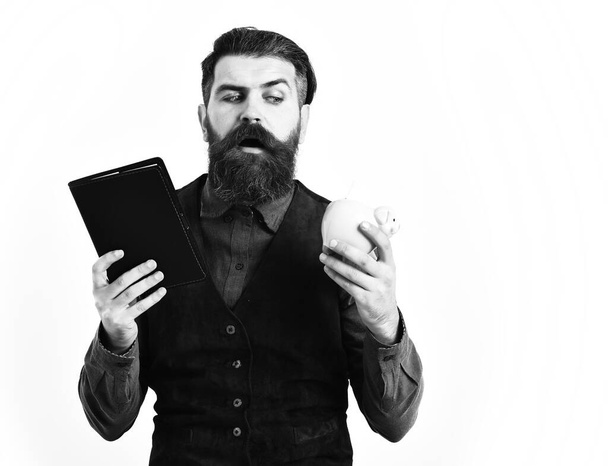 bearded man holding notepad and moneybox with serious face - Fotoğraf, Görsel