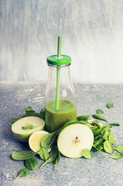 Green smoothie in bottle and ingredients: apple and spinach, on rustic background, front view, retro toned.  Healthy, diet or detox beverage concept - Photo, image