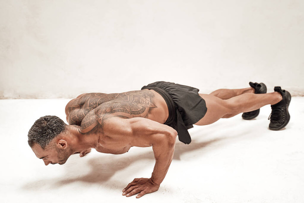 Męski sportowiec odizolowany na białym tle w spodenkach sportowych wykonujących ćwiczenia pomostowe brzucha - Zdjęcie, obraz