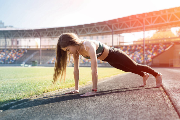 Young sportive woman making morning exercises outdoors on the stadium - Foto, imagen