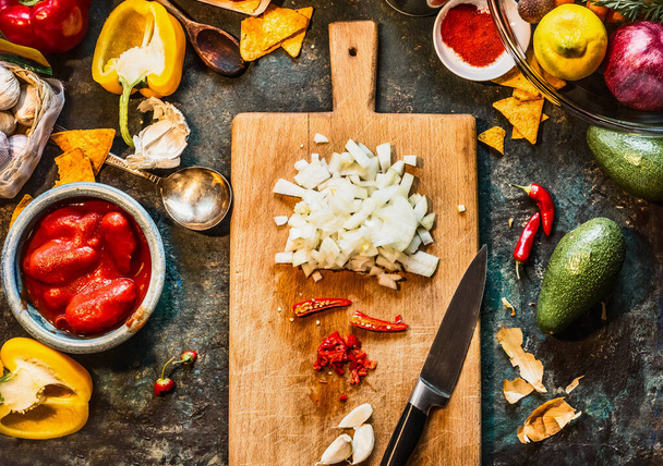 Chopped spices on wooden cutting board with knife: chili, onion and garlic  with vegetables ingredients for Mexican cuisine on dark rustic kitchen table, top view - Fotoğraf, Görsel