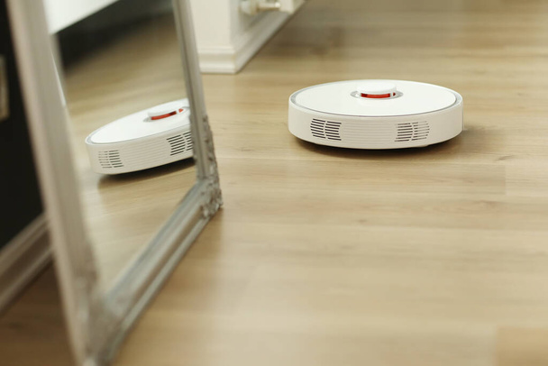white robotic vacuum cleaner. The robot is controlled by voice commands for direct cleaning. Modern technology of smart cleaning. scheduled cleaning of the apartment. selective focus. - Foto, Imagem