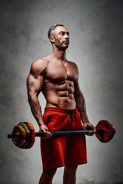 Masculine sportsman isolated on the white background wearing sport clothes showing his athletic body with naked torso, looking motivated and holding a barbell - Photo, Image