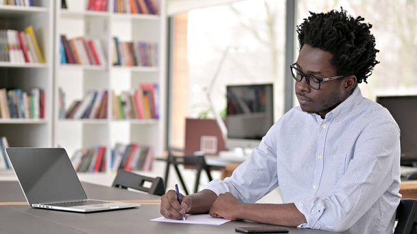 Afrikaner schreibt bei der Arbeit auf Papier - Foto, Bild