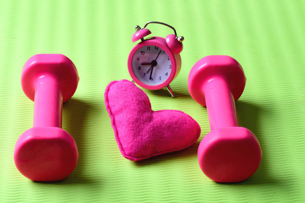 Morning workout concept. Dumbbells in pink color near alarm clock - Foto, Imagem