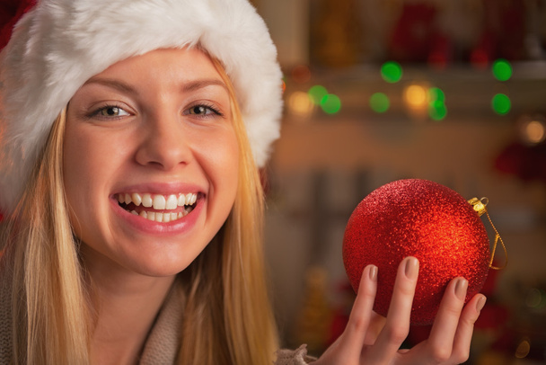 Portrait of happy teenage girl in santa hat showing christmas ball - Foto, imagen