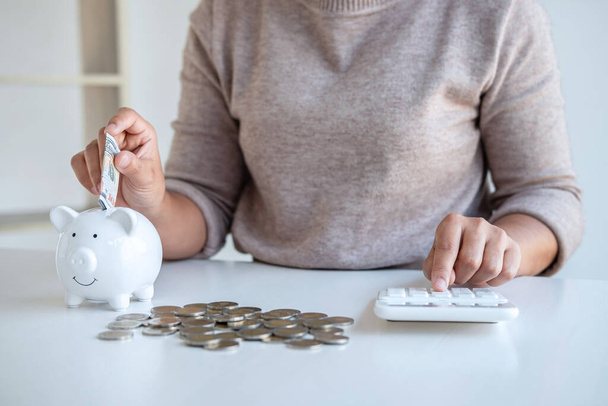 Young woman putting money into piggy bank planning growing saving to strategy and calculating with money box for future plan fund of travel, education, home and retirement. - Photo, Image