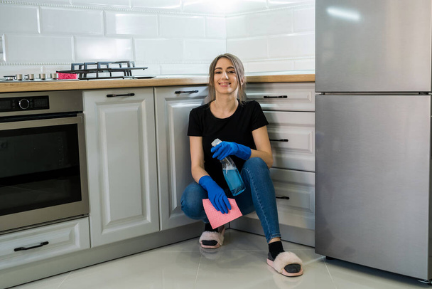 Sonriente niña adulta limpieza cocina con botella de aerosol y un paño de microfibra
 - Foto, Imagen