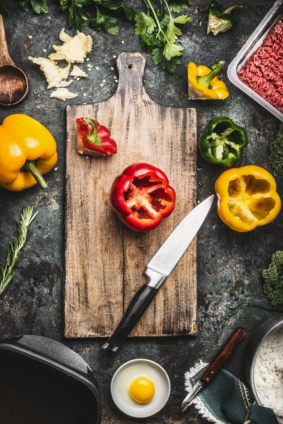 Bell colorful paprika peppers cooking preparation. Paprika on wooden cutting board with kitchen knife, minced meat, egg and seasoning on dark rustic background, top view - Foto, imagen