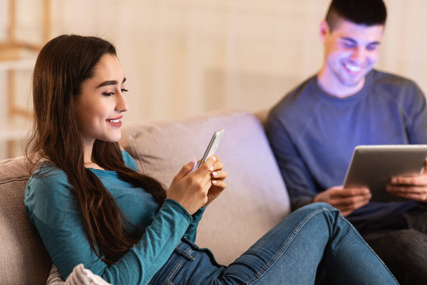 Couple sitting on couch using tablet and cell phone - Fotó, kép