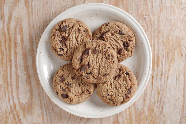 Čokoládové sušenky na talíři na dřevěném pozadí, pohled shora - Fotografie, Obrázek