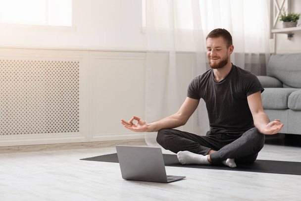 Millennial guy meditating with trainer online via laptop - Fotoğraf, Görsel