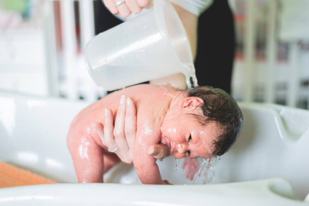 Mom soaks the baby with shampoo. Concept first bathing newborn baby - Foto, imagen