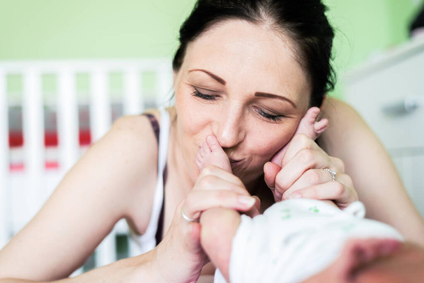 Beautiful mom with emotional expresion face supports and tenderly cuddles the newborn baby gently while the infant is lying on bed.Caucasian  mother looking at the baby with love and showing protection. - Foto, Bild