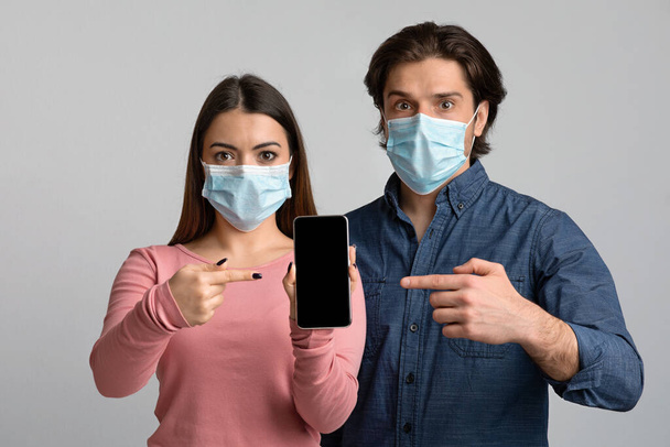 Couple choqué dans les masques médicaux pointant vers Smartphone avec écran noir
 - Photo, image
