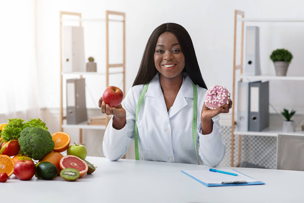 Hezká dietní doktorka drží v rukou koblihu a jablko - Fotografie, Obrázek