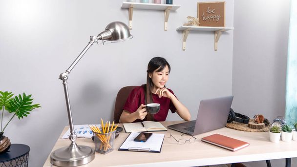 Pensivo mulher asiática está relaxando na área de trabalho remotamente a partir de casa com laptop para se comunica na internet com o cliente, E aprender a ensinar no chat online, quarentena conceito Coronavirus
 - Foto, Imagem