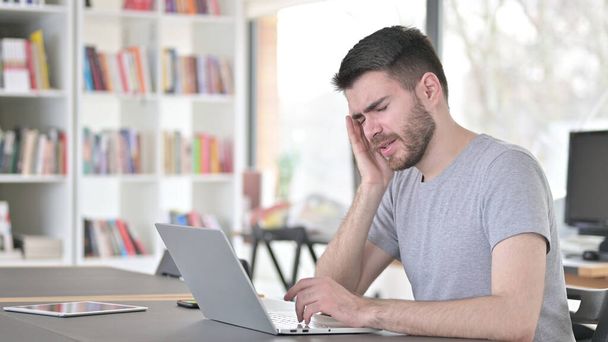 Jovem com dor de cabeça usando laptop no escritório
 - Foto, Imagem
