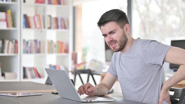 Dizüstü bilgisayarı olan genç adam ofiste sırt ağrısı çekiyor. - Fotoğraf, Görsel