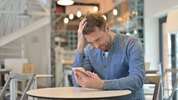 Upset Casual Man having Loss on Smartphone in Cafe - Photo, Image
