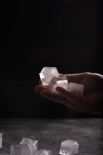 Мужская рука с кубиками льда, разбросанным по столу льдом. Атмосферное тёмное изображение
 - Фото, изображение