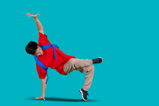 Attractive boy doing freestyle dance in the studio while carrying bag with blue background - Foto, afbeelding