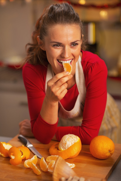 Happy young housewife eating orange in christmas decorated kitchen - Foto, immagini
