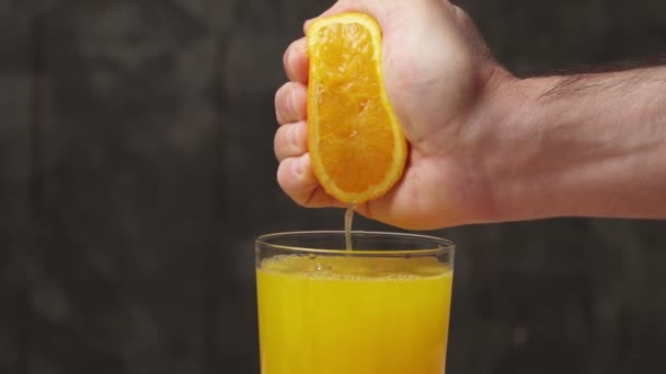 Ręcznie wyciska pomarańczowy owoc do szklanki, z bliska, tworząc pełną szklankę świeżego soku pomarańczowego - Materiał filmowy, wideo
