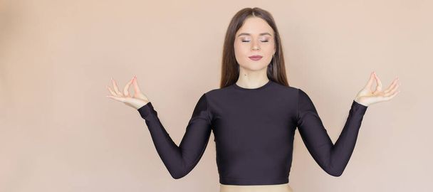 The girl holds her fingers in a "mudra" position and relents with her eyes closed. A young woman on a beige one-ton background. - Foto, imagen