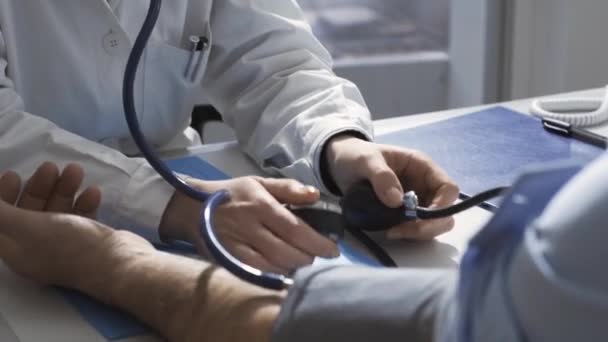 Female doctor measuring blood pressure of a patient and smiling - Felvétel, videó