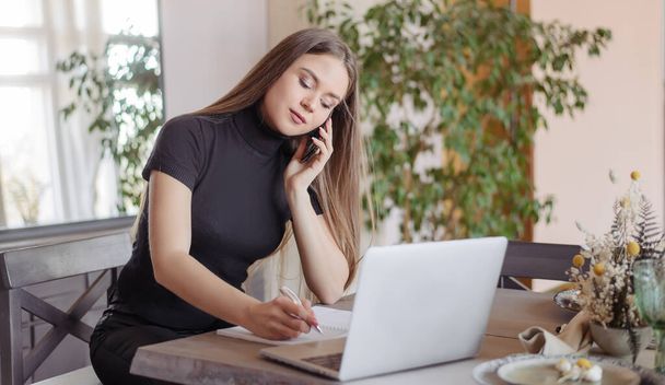 Девушка работает дома за компьютером и ноутбуком онлайн. Молодая женщина залезла в интернет. Она пишет в блокноте и говорит по телефону.
. - Фото, изображение
