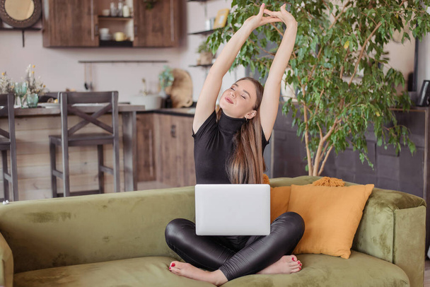 La chica trabaja en casa con una computadora y un portátil. Una mujer joven navegar por Internet en línea. Ella levanta las manos, tira mientras descansa, se siente cansada
. - Foto, imagen