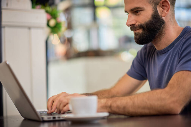 Fiatal szakállas kaukázusi férfi ül az étteremben, és a laptop. - Fotó, kép