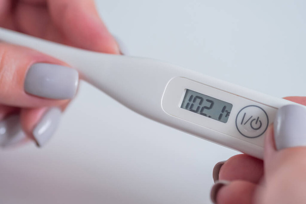 Close up: woman hands holding white digital medical thermometer with high temperature - selective focus. Healthcare, diagnostic, measurement, disease, infection, coronavirus concept - Photo, Image