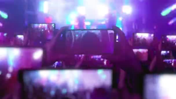 The crowd watches a concert, sings, jumps. Strobing stage lights. Happy people. Musical concept. Fans are recording videos on smartphones. A lot of smartphones. Live Stream. Stories.  - Footage, Video
