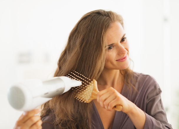 Happy woman brushing and blow drying hair in bathroom - Photo, Image