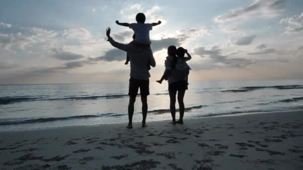 Família asiática feliz nas férias de verão Crianças nas costas pais e mãe Olhando para o céu e mãos onduladas na praia Fundo pôr do sol no mar. Relaxe o conceito de férias e viagens. Movimento lento
 - Filmagem, Vídeo