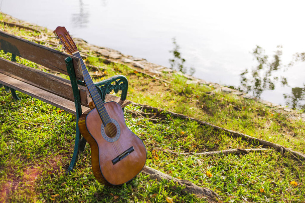 guitar acoustic standing beside wood bence in the parks and light of sunset. - Fotó, kép