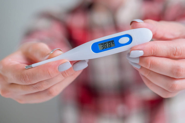 Frauenhände zeigen weißes digitales medizinisches Thermometer mit hoher Temperatur - Nahaufnahme, selektiver Fokus, Frontansicht. Gesundheitswesen, Messung, Krankheit, Covid 19, Infektion, Coronavirus-Konzept - Foto, Bild
