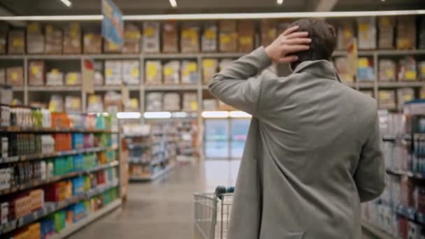 Giovane uomo in maschera protettiva a piedi tra diverse sezioni nel grande negozio di alimentari
 - Filmati, video