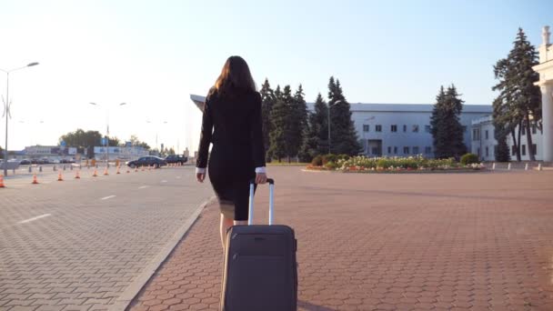 Donna d'affari irriconoscibile con valigia cammina verso l'aeroporto per andare in viaggio d'affari. Signora in scarpe tacchi alti passo con il suo bagaglio lungo la strada. Concetto di viaggio. Retrovisore rallentatore Close up - Filmati, video