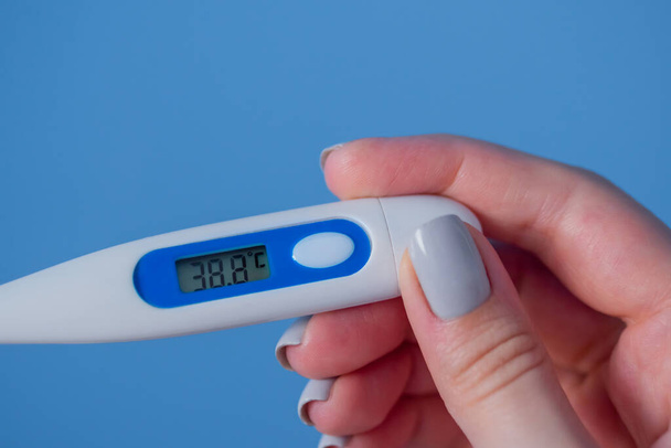 Женщина держит за руки белый цифровой медицинский термометр с высокой температурой - близкий обзор, избирательный фокус. Здравоохранение, здравоохранение, болезни, инфекции, коронавирус - Фото, изображение