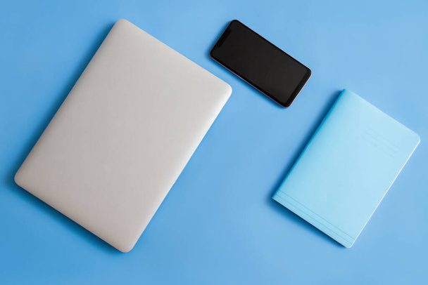 青い背景にノートパソコン。青い背景にノートパソコンとボトル。青い背景にノートパソコンの電話とメモ帳。ノートパソコン、ノートパッド、青い背景のボトル.  - 写真・画像