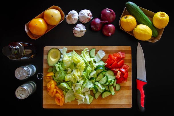 Salade tranchée, concombres, tomates. Légumes sur une planche à découper. Tomates jaunes, oignons bleus, citrons, concombres
. - Photo, image
