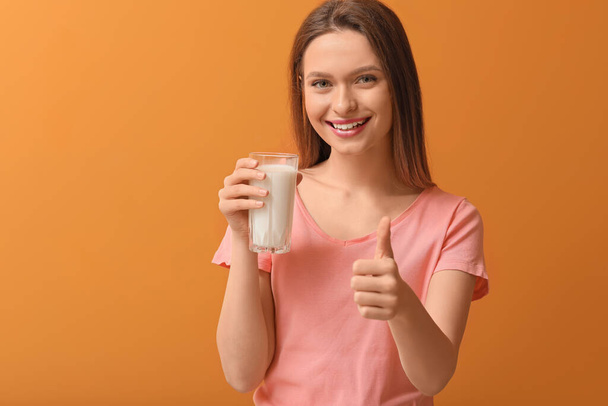 Young woman with glass of milk showing thumb-up gesture on color background - Foto, Bild