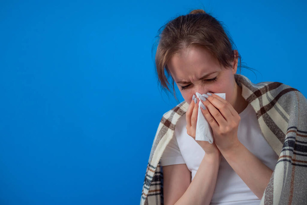 Женщина чувствует себя больной, чихает в ткань лица против синей стены дома
 - Фото, изображение